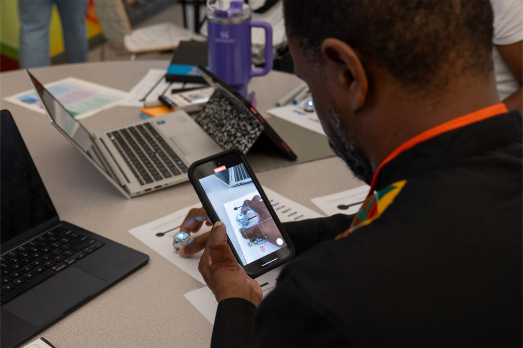 A man looks at his phone screen which captures a ball he is placing on the table in front of him.