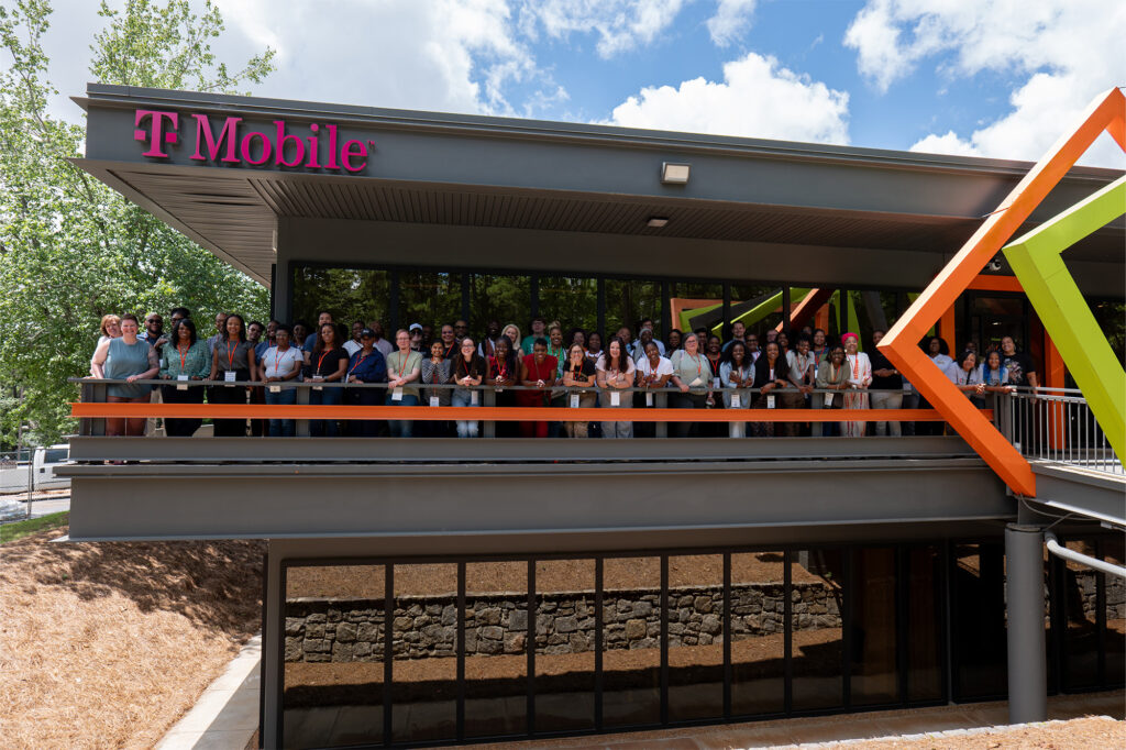 Group photo of several dozen people posing on a balcony on a building ordained with the T-Mobile logo.