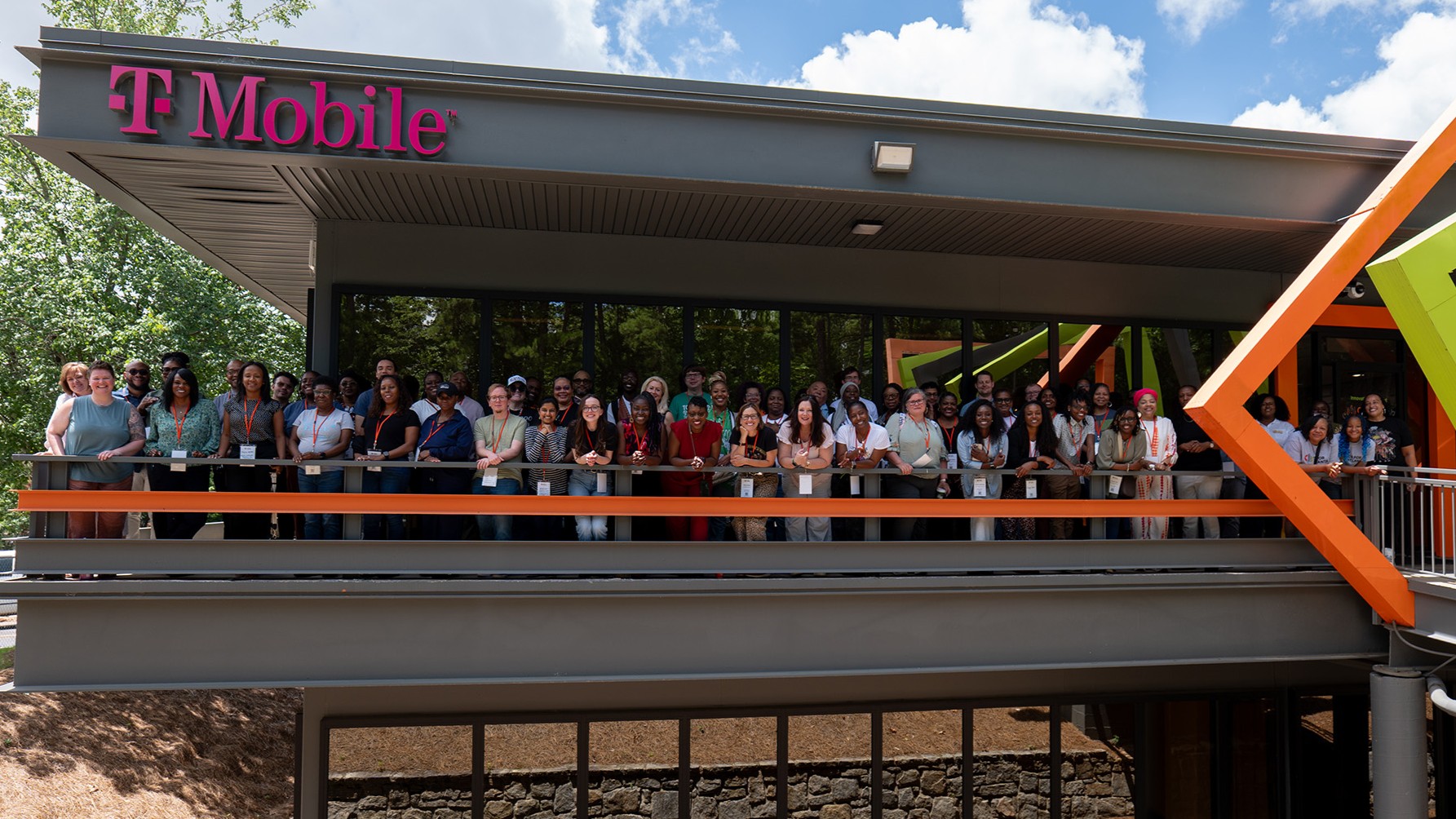 Group photo of several dozen people posing on a balcony on a building ordained with the T-Mobile logo.