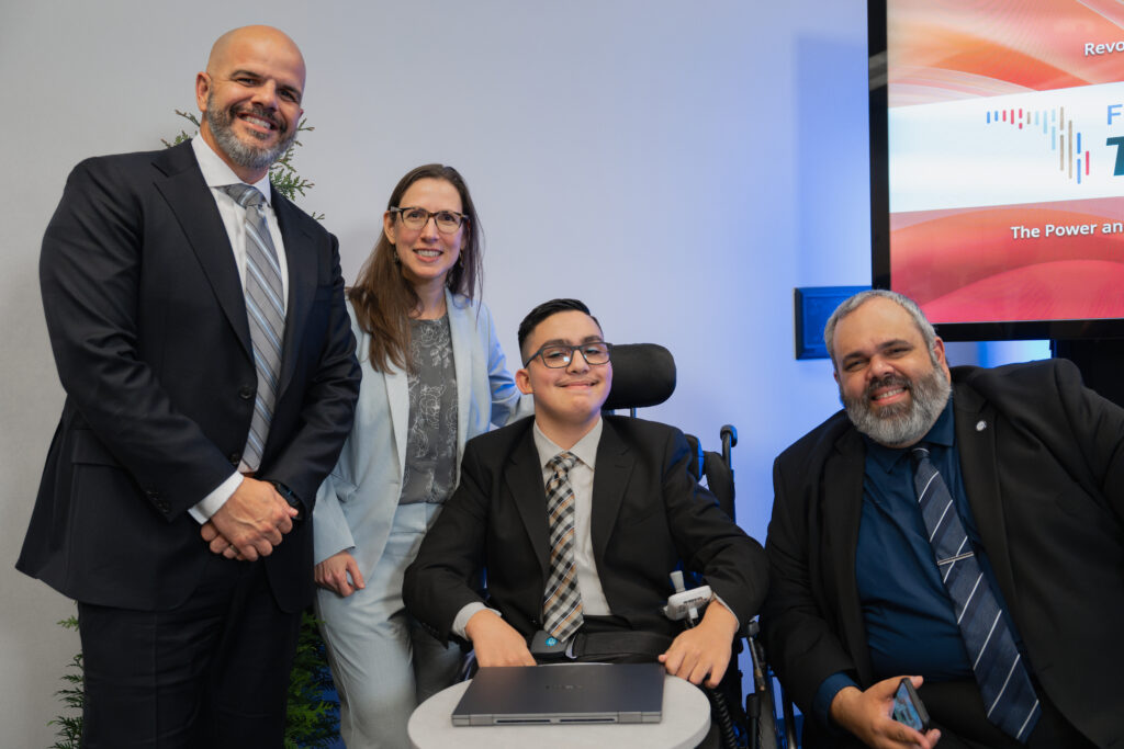 2 men and 1 woman stand behind a young standing girl and a boy in a wheelchair as all 5 smile at the camera.