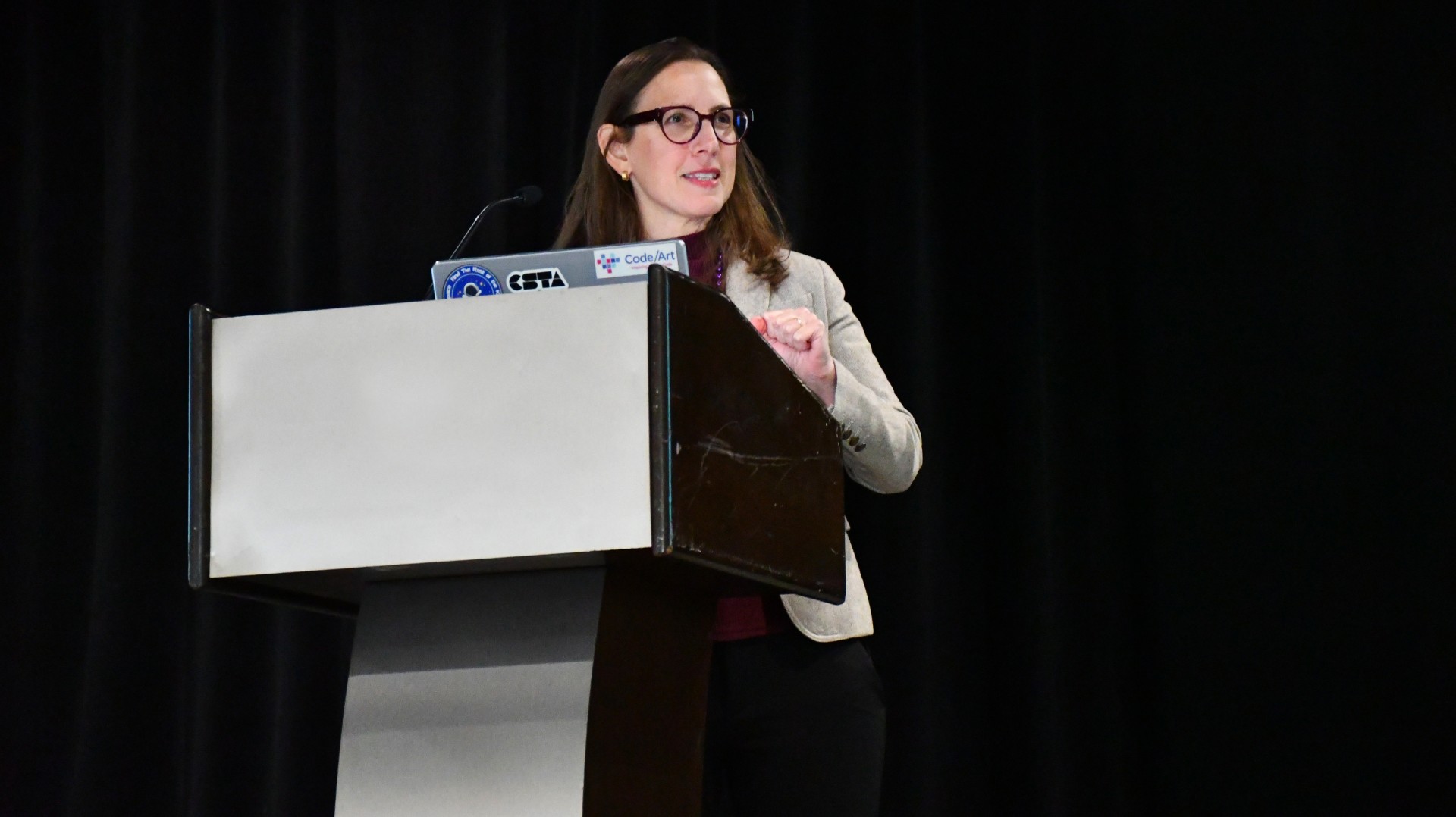 Untitled Maya Israel standing in front of a blank curtain at a podium with her computer presenting.