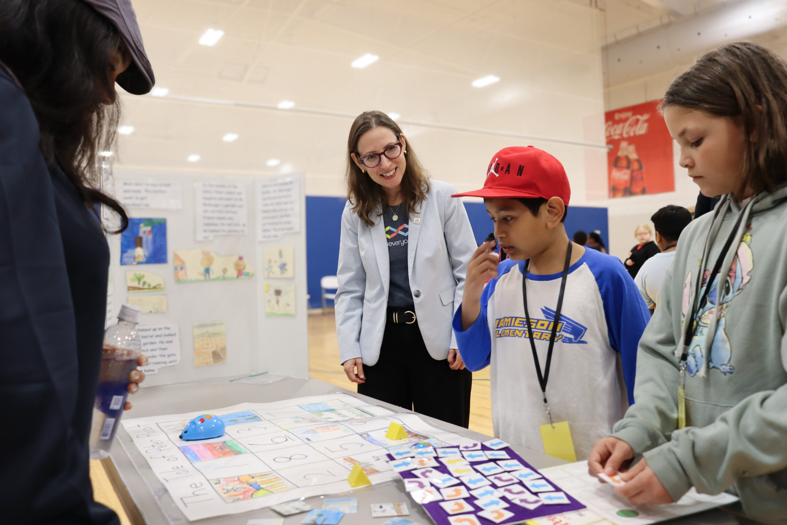 Maya Israel at table with students looking over poster board presentation and learning tools.
